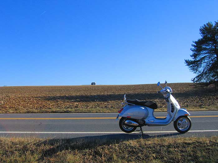 Vespa GTS scooter parked along a rural road.