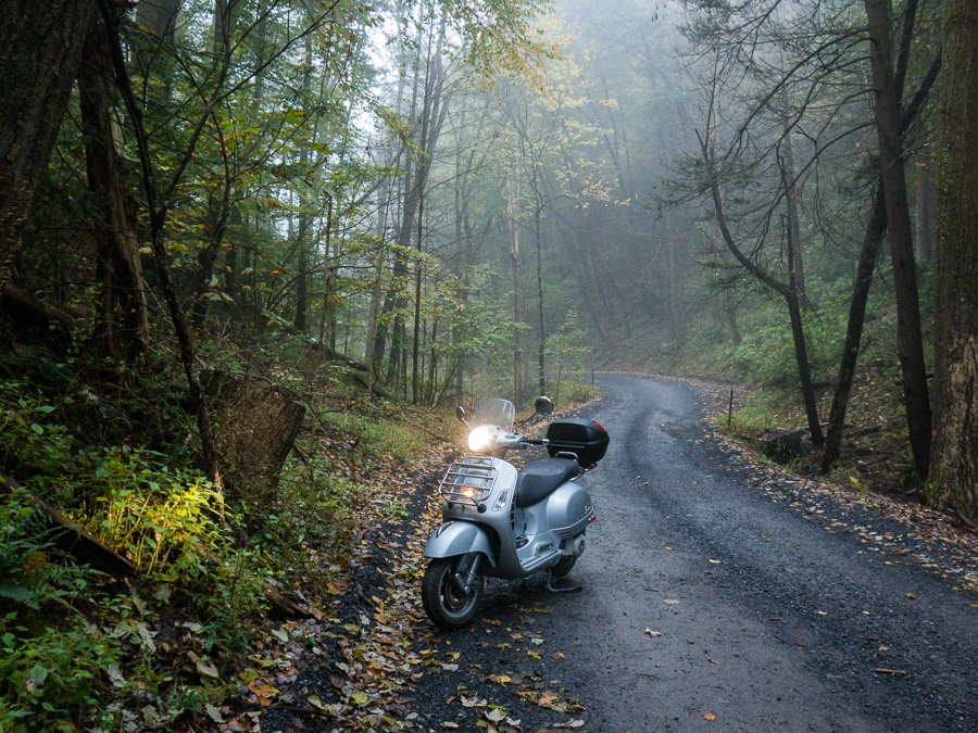 Vespa GTS scooter on a gravel forest road in the fog