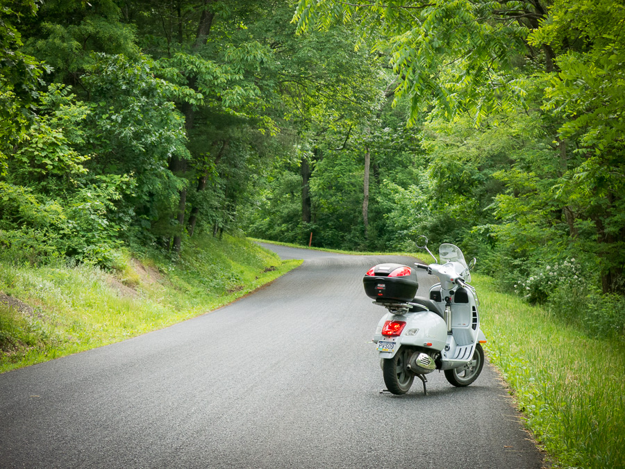 Vespa GTS scooter along wooded road.