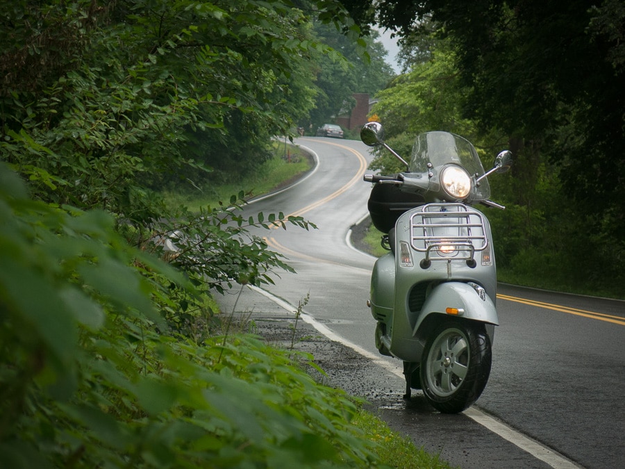 Vespa GTS scooter on a wet, rural road.