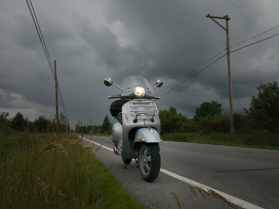 Vespa GTS on the road with an approaching rain storm.