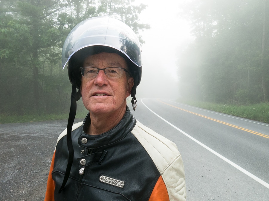 Man with motorcycle helmet on a foggy road.