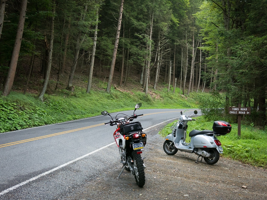 A motorcycle and scooter parked along a road in a forest