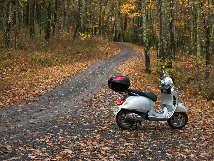 Vespa GTS scooter along a gravel forest road.