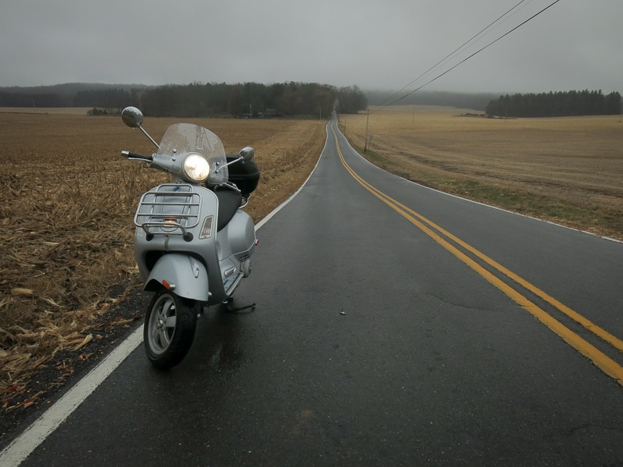 Vespa GTS scooter on a long, wet country road.