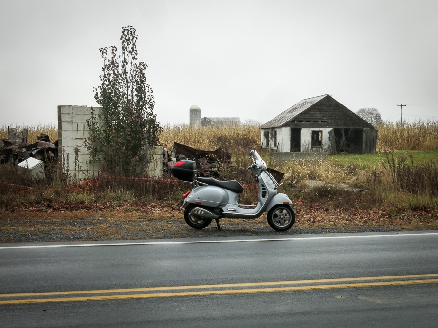 Vespa GTS scooter parked near a decaying barn.