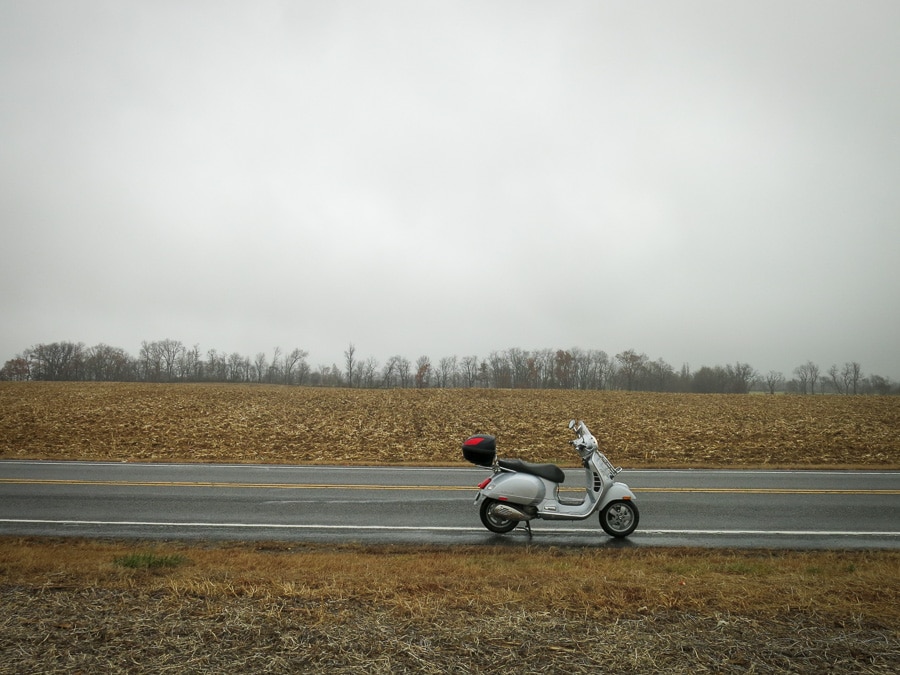 Vespa GTS scooter on a rural road with empty fields.