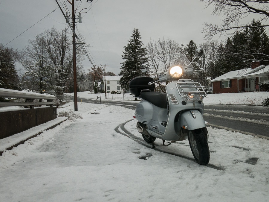 Vespa GTS scooter stopped along a snowy street.