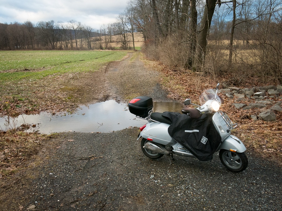 Vespa scooter on a farm land next to a small creek.