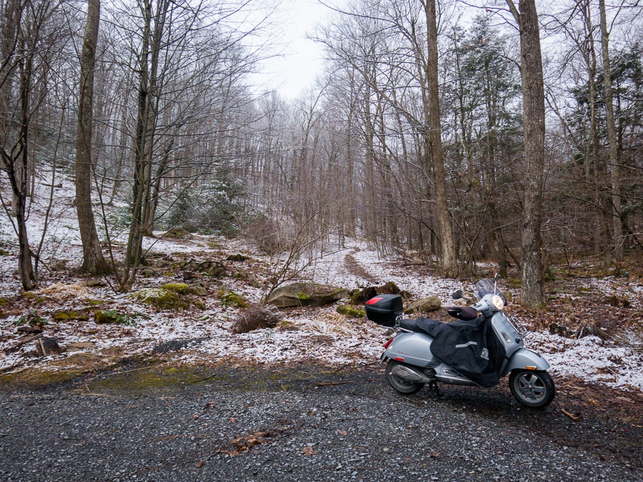 Vespa scooter on a gravel forest road with snow.