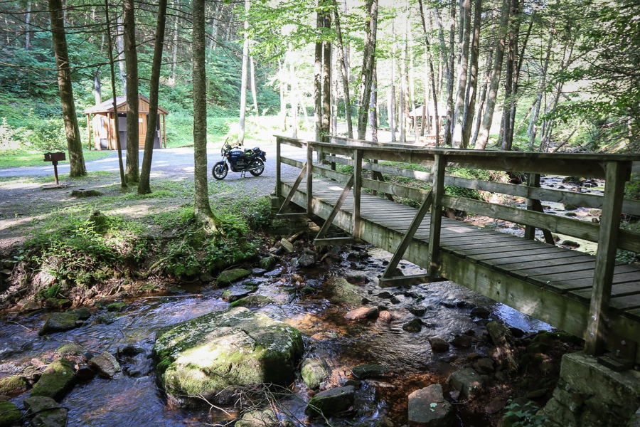 Motorcycle parked near a wooden bridge in a picnic area.
