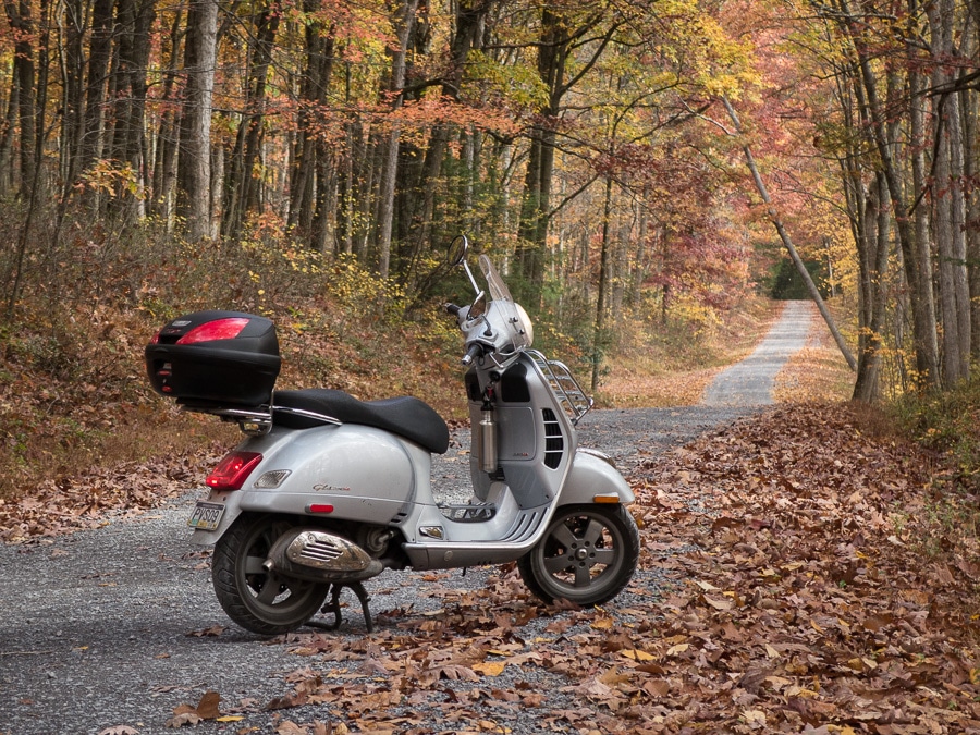 Vespa GTS scooter on a gravel forest road.