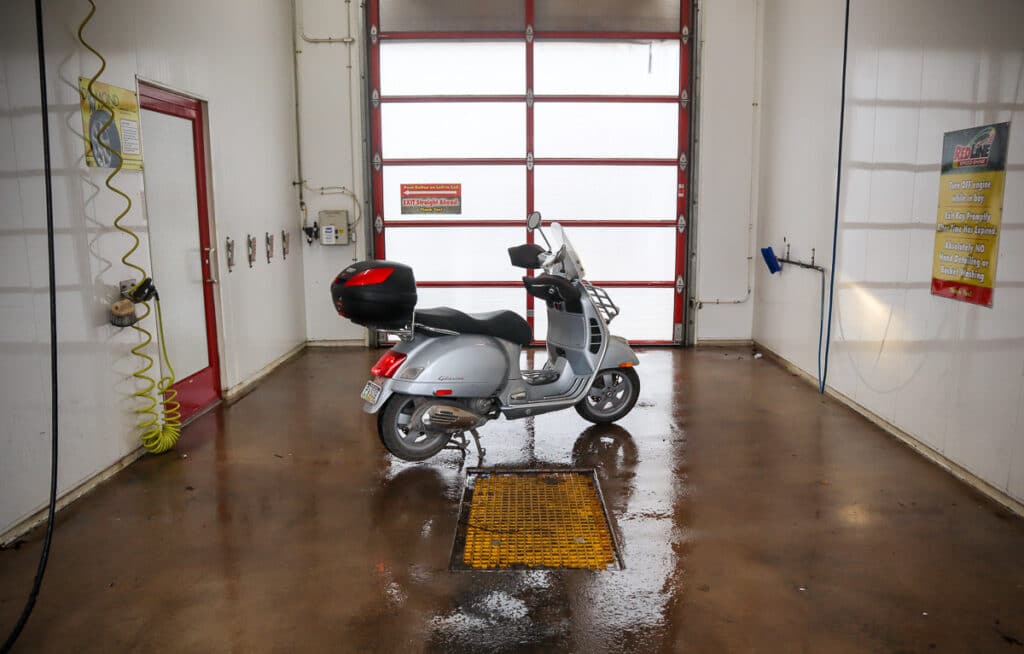 Vespa GTS scooter in a self-service car wash bay.