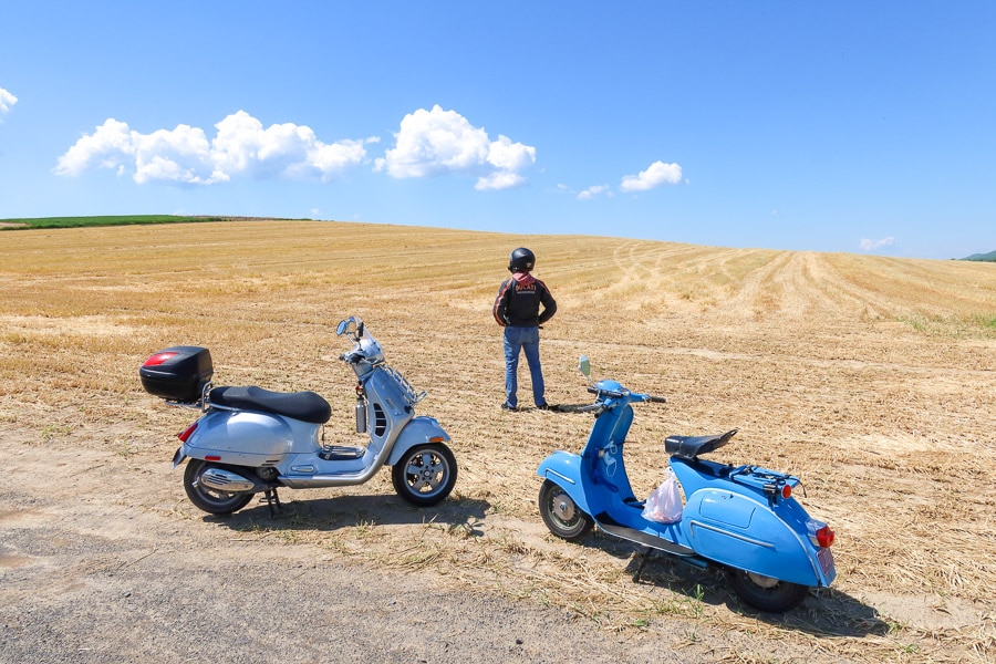 A modern and vintage scooter parked in a farm field.