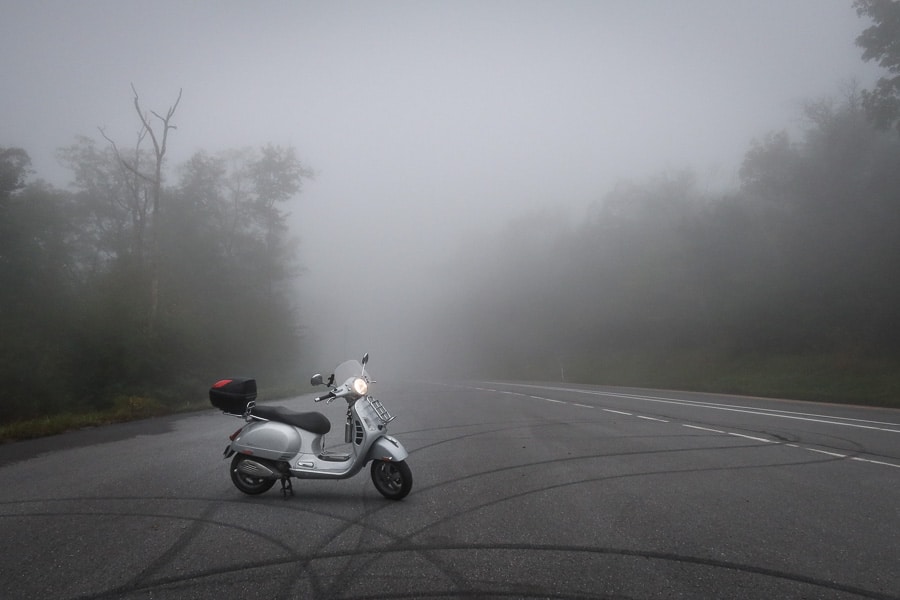 Vespa GTS scooter parked along a road with dense fog.