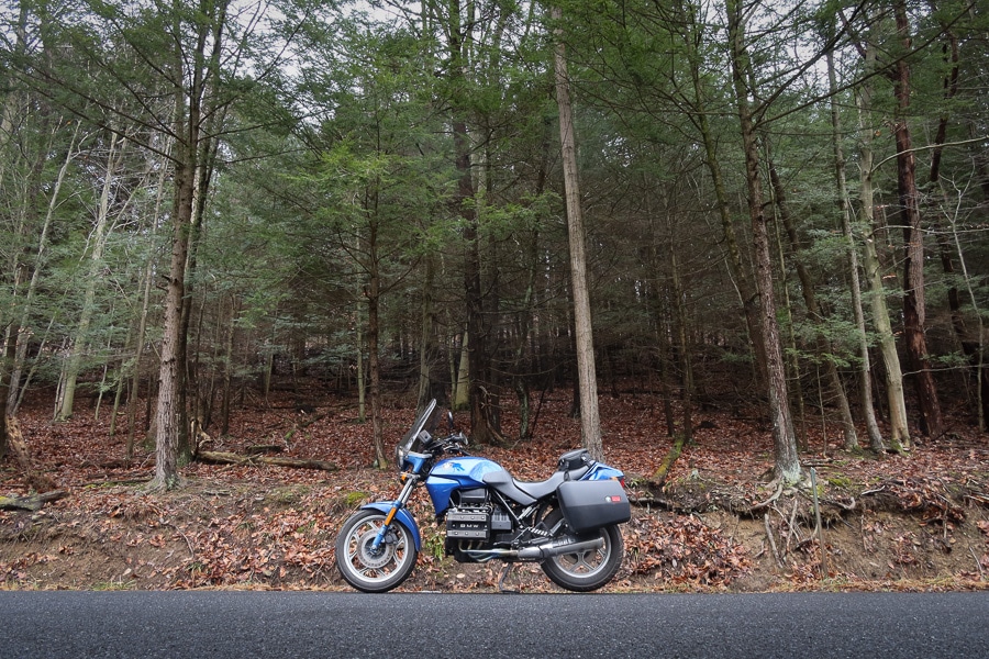 1992 BMW K75C motorcycle on a road in a forest.
