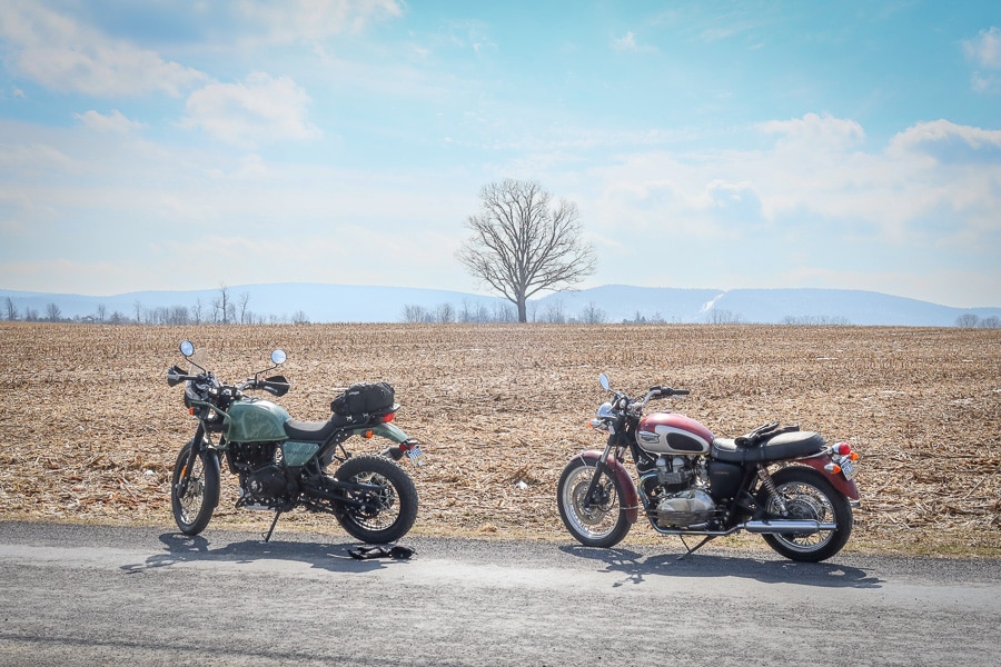 Two motorcycles parked by a farm field.