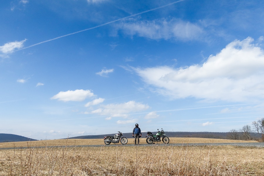 A man and two motorcycles standing in a field.
