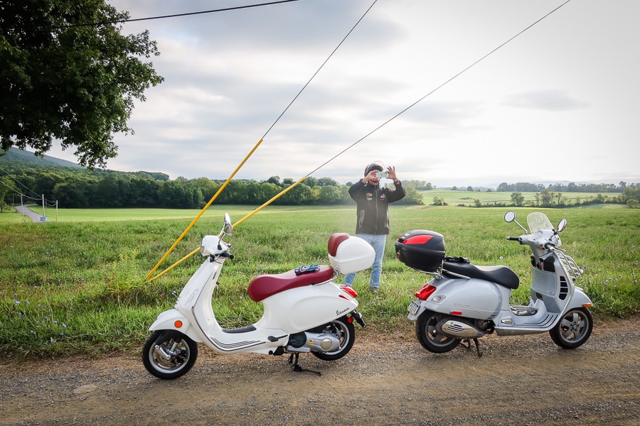 Two Vespa scooters stopped along a rural road.