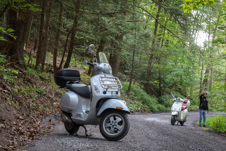 Two Vespa scooters stopped along a gravel mountain road.