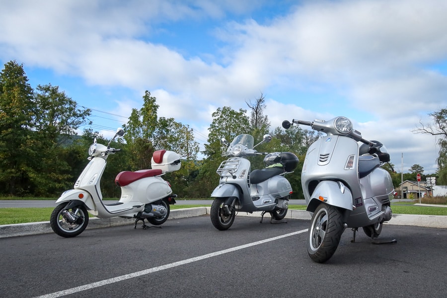 Three modern Vespa scooters in a parking lot.