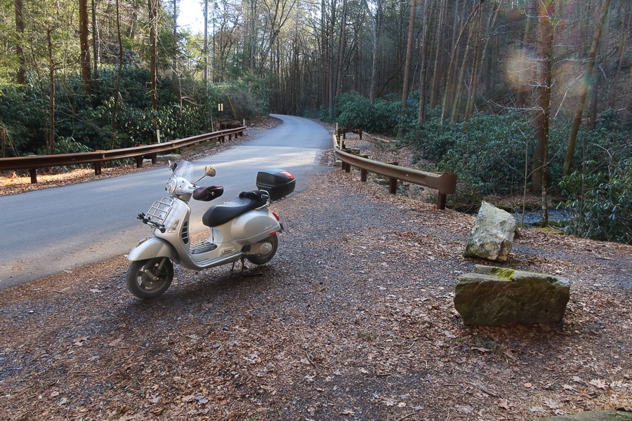 Vespa GTS 250 scooter parked along a forest road.