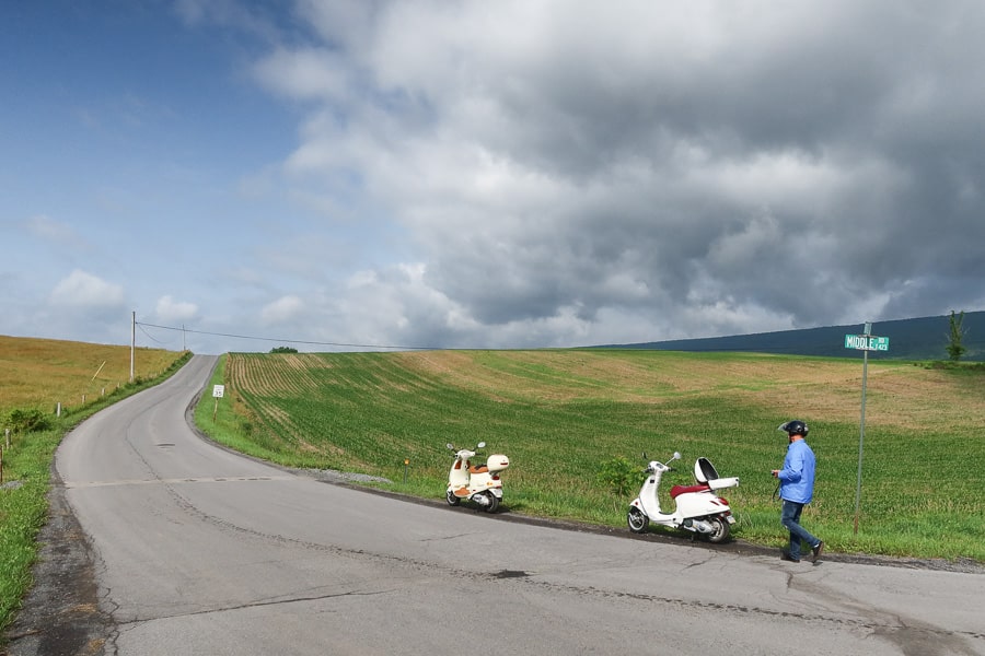 Two Vespa scooters along a rural road.