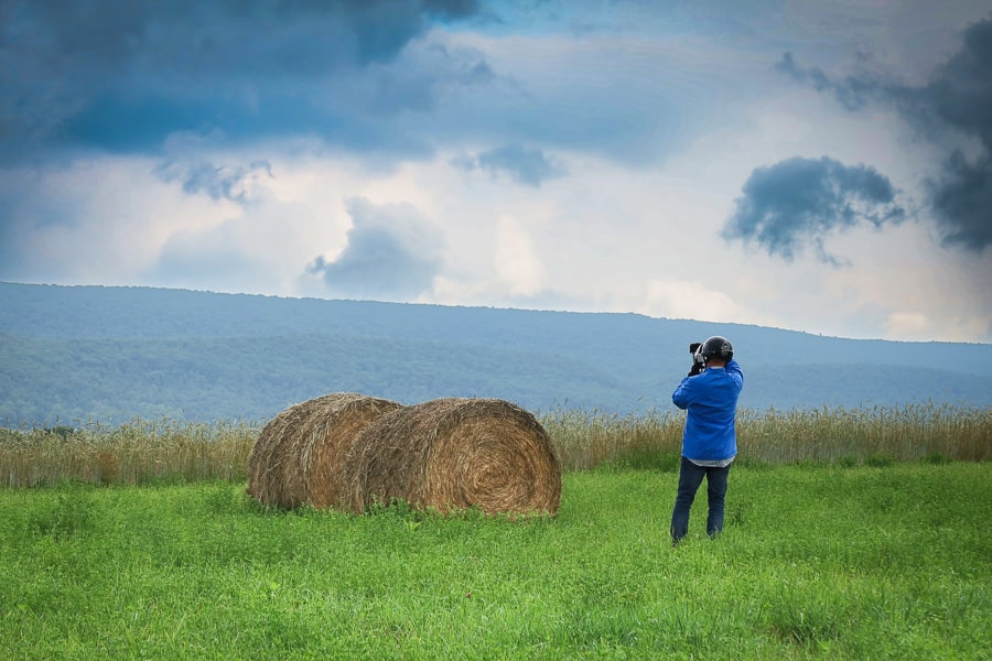 Man photographing round bales in a field.
