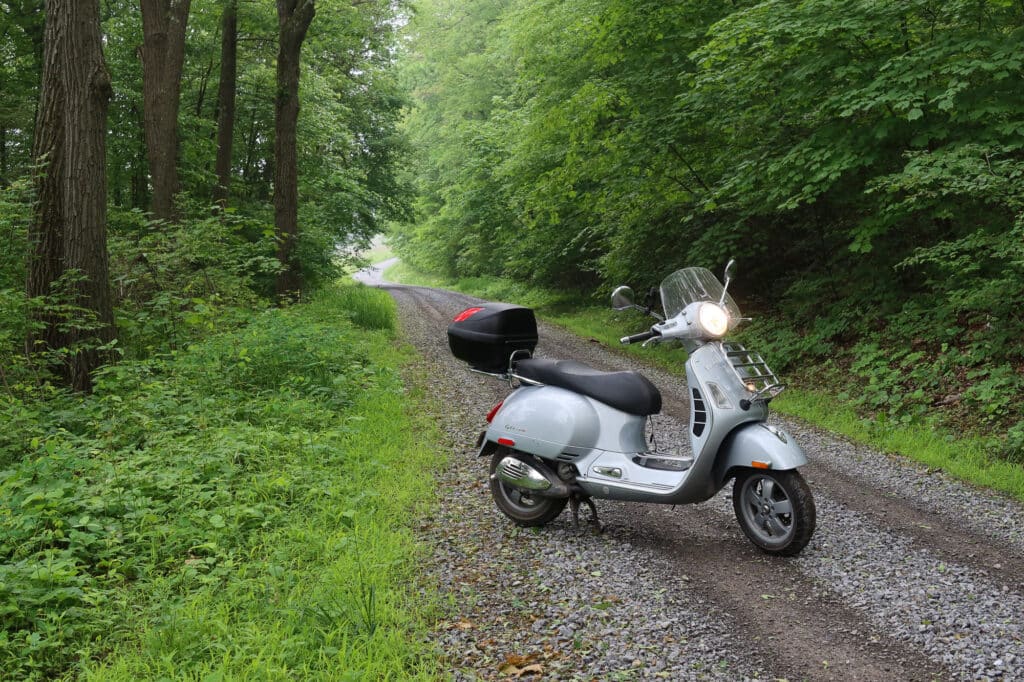 Vespa GTS scooter on a gravel forest road.