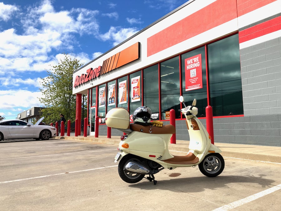 Vespa scooter parked at an auto parts store.