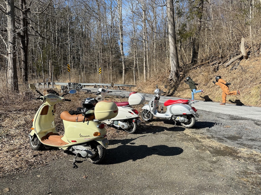 Three Vespa scooters along a rural road.