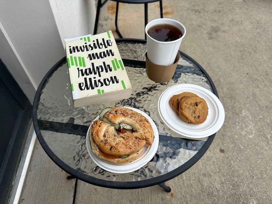 tea, bagel, and book sitting on a table at an outdoor cafe.