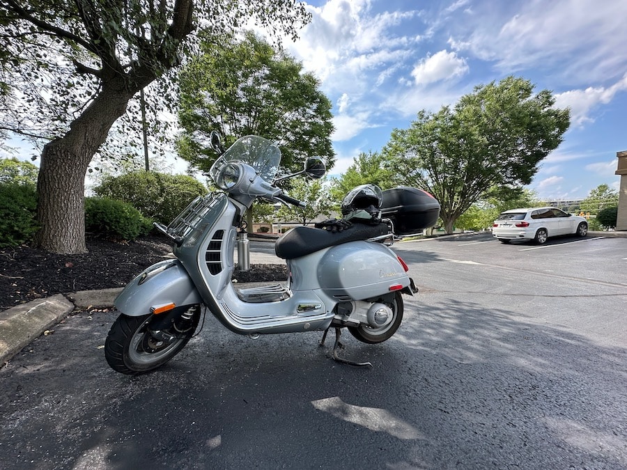 Vespa GTS scooter parked in the shade in a bank parking lot.