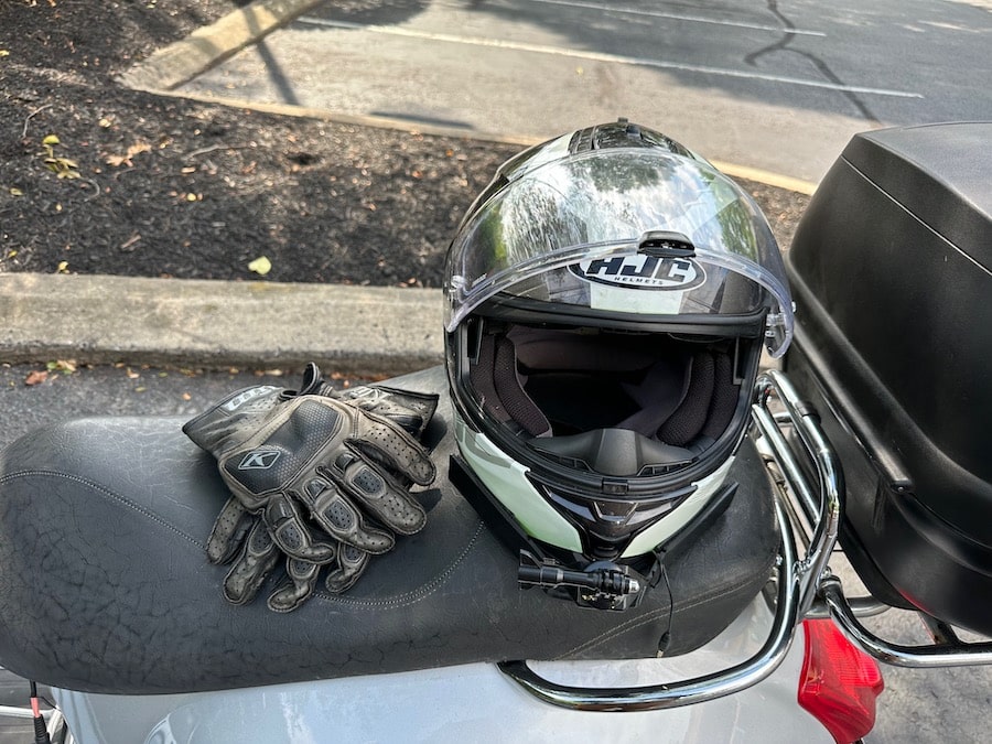 Motorcycle and gloves on the seat of a Vespa GTS scooter.