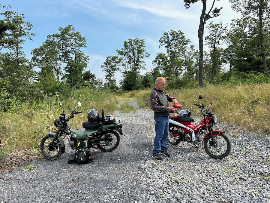 Two Honda Trail 125 motorcycles at a stop for coffee on a gravel road.