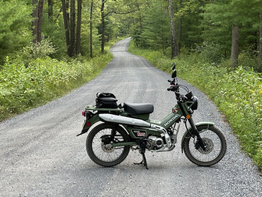 2023 Honda Trail 125 parked along a gravel forest road.