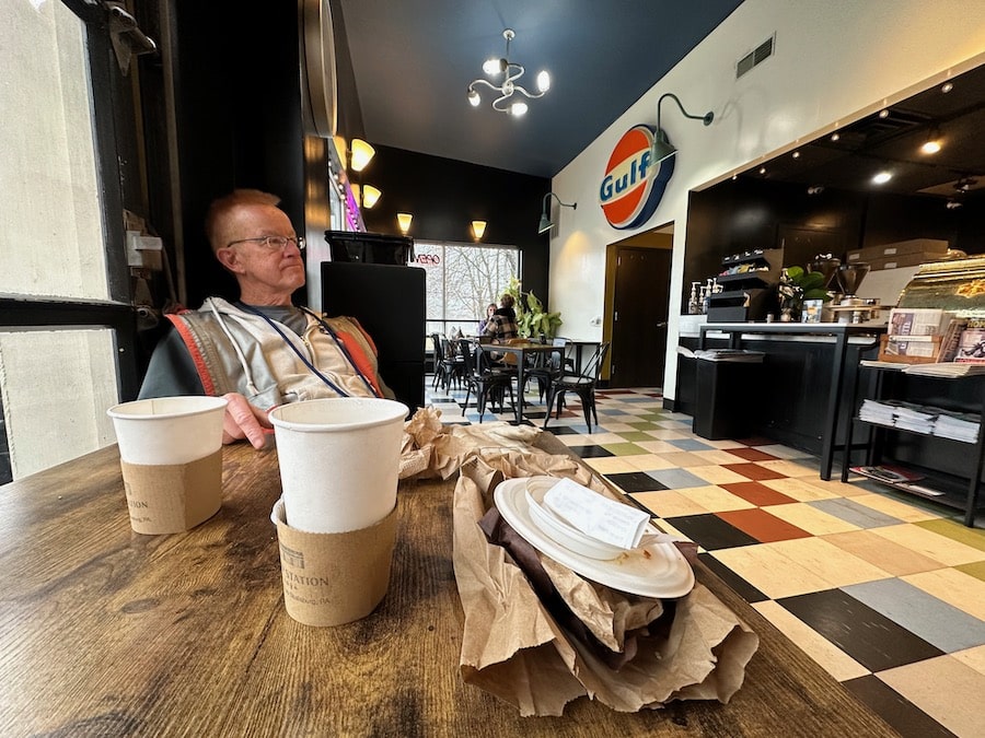 Guy sitting in a cafe with a table of trash.