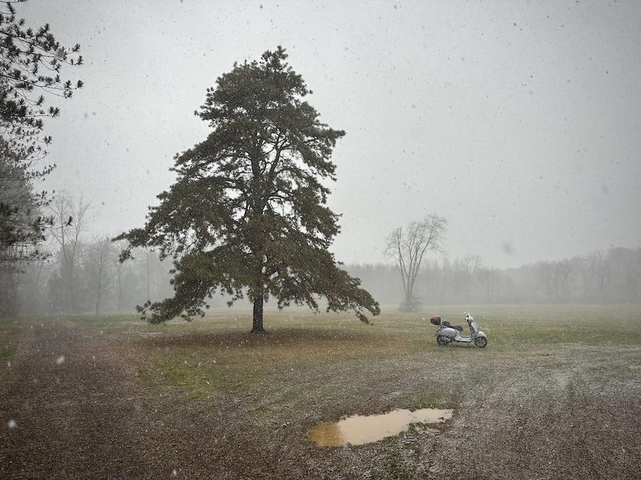 A 2006 Vespa GTS 250 scooter parked in a field as it begins to snow.