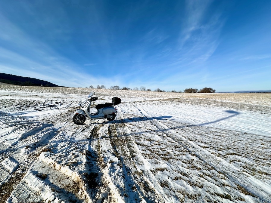 A Vespa GTS scooter parked on a snow covered field.