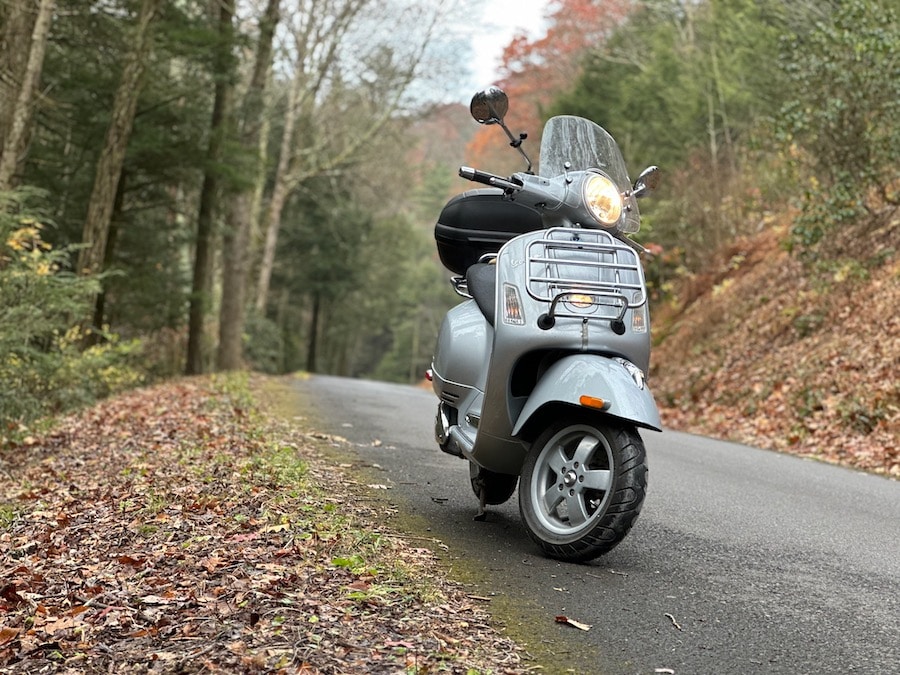Vespa GTS scooter on a paved forest road.
