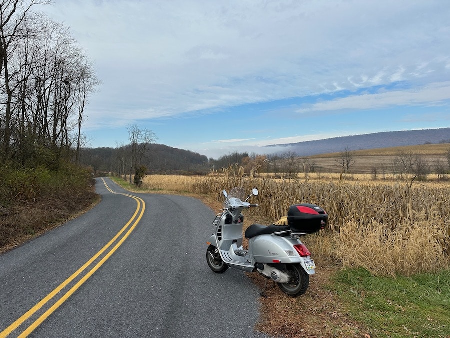 Vespa GTS scooter parked along a rural road.