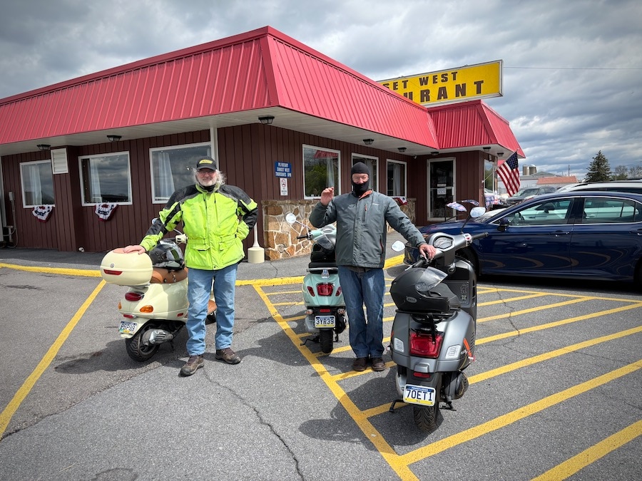 Two men standing with their Vespa scooters.