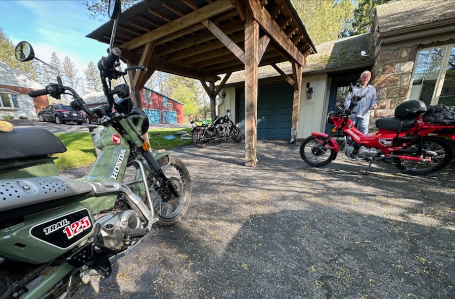 Two Honda Trail 125 motorcycles in a driveway.