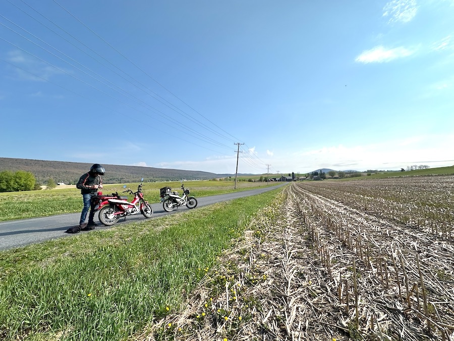 Two Honda Trail 125 motorcycles parked along a rural road.