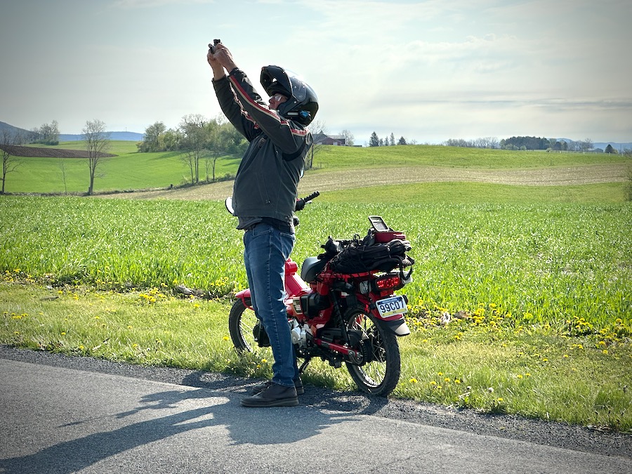 Motorcycle rider standing by his bike making a photograph while holding the camera high over his head.