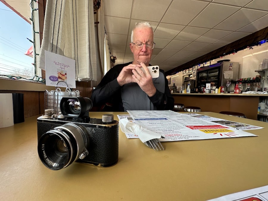 Leica I sitting on a table in a dinner while a man makes a photo with an iPhone.
