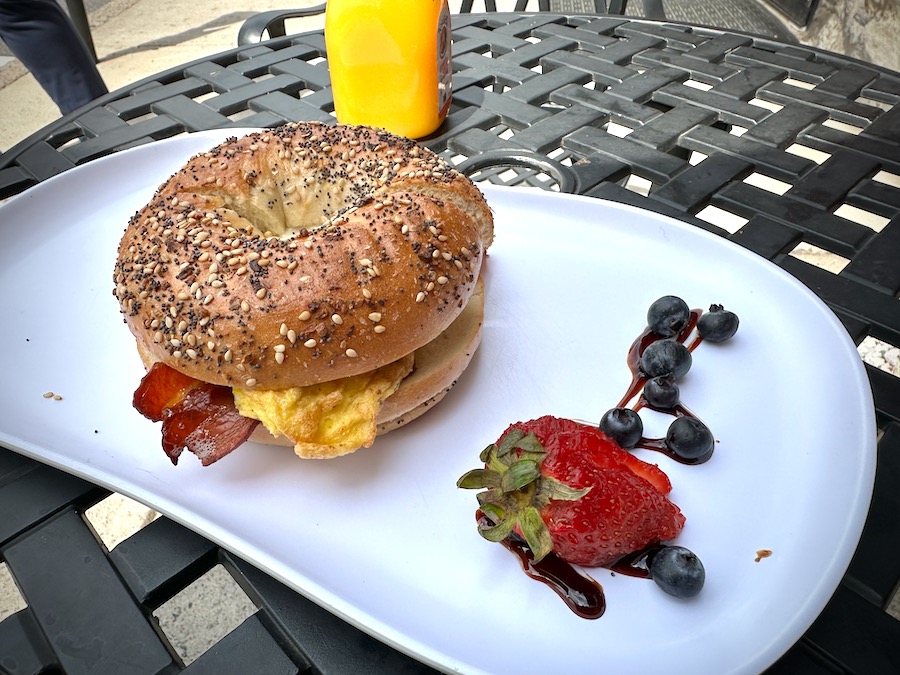 A breakfast sandwich on a white place with a strawberry.