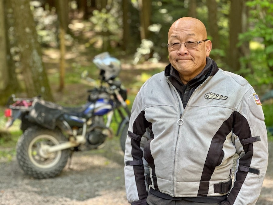 Portrait of Dom Chang with his Yamaha TW200 motorcycle in the background.
