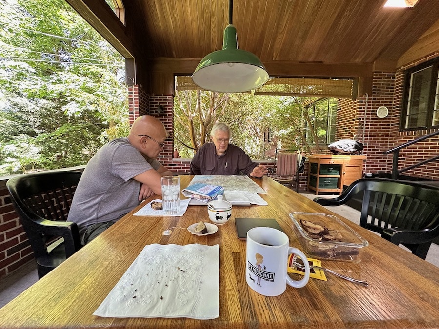 Two men looking at maps at an outdoor table.