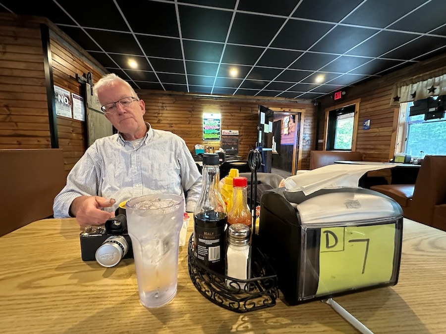 Man sitting at a table in a restaurant with an old Leica camera on the table.
